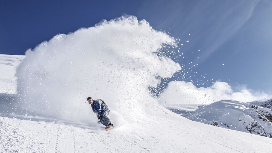 Man snowboarding down a mountain with a big cloud of snow behind him
