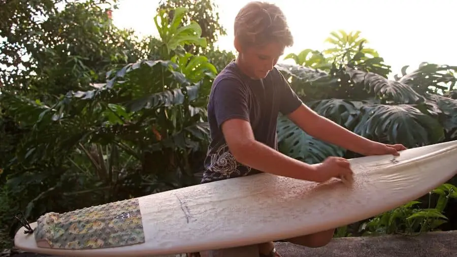 Boy waxing his surfboard